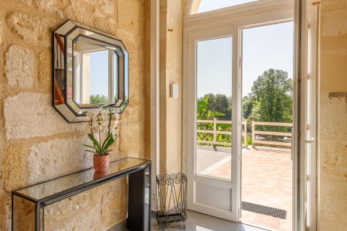 Elegant entryway at Domaine De Pimpine cottage with stone walls, decorative mirror, potted plant, and French doors opening to