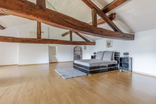 Spacious loft bedroom at Domaine De Pimpine cottage with exposed wooden beams, bed, and wooden flooring in Galgon