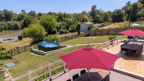 Riverside cottage terrace at Domaine De Pimpine with red umbrellas, pool, and river views in Galgon, France