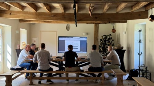 Group meeting in Cloffy's reception hall with exposed beams, flat-screen TV, and modern workspace in Nouans-les-Fontaines