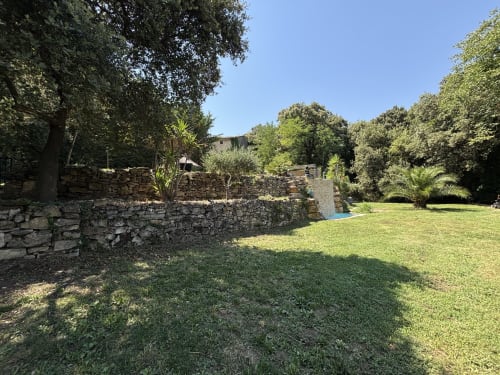 Jardin aux murs de pierre avec gazon verdoyant et arbres à Mas Provençal, gîte en Provence à Bollène