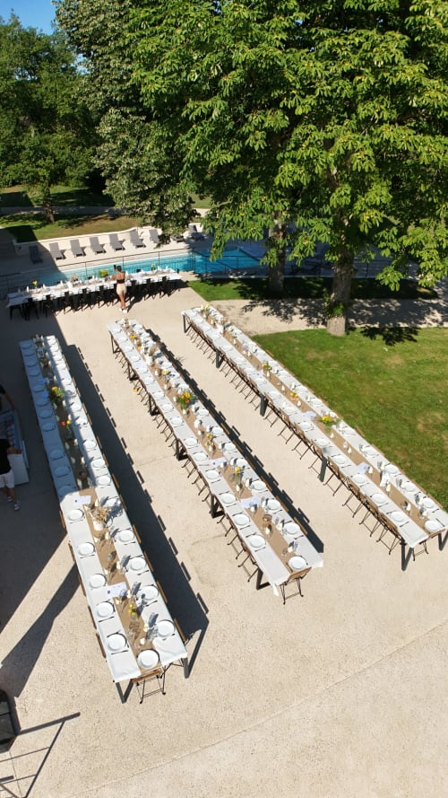 Aerial view of long dining tables set up on patio at Vindihouses Épinac, with pool and trees beyond