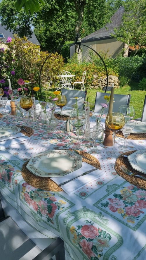 Table d’hôtes dressée dans le jardin de Ty Coz Breizh à Guidel, en Bretagne Sud, avec nappe fleurie, vaisselle élégante, verres colorés et petits bouquets de fleurs fraîches.
