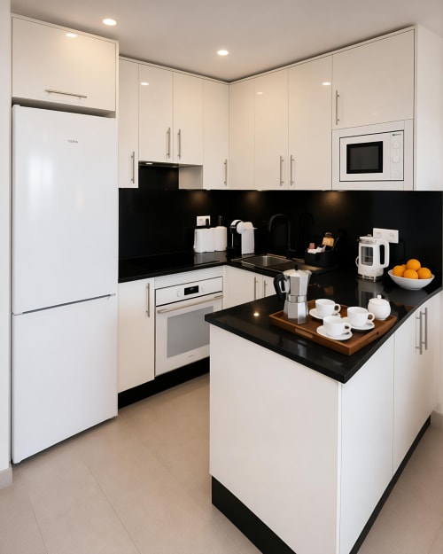 Modern white and black kitchen with island, stainless steel appliances, and black backsplash in Manage Home Tenerife luxury