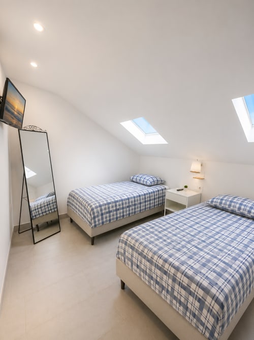 Bright attic bedroom with two single beds, blue checkered bedding, skylight windows, and mirror at Manage Home Tenerife