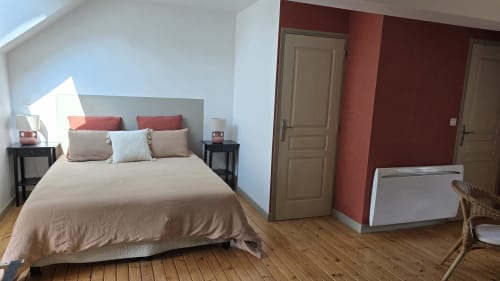 Chambre lumineuse au Domaine de la Cour VAUTIER avec literie beige, touches rouges, parquet et vue jardin près d'Omaha Beach