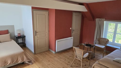 Spacieuse chambre au Domaine de la Cour Vautier aux murs rouges, parquets en bois, deux lits, fauteuils en rotin et vue sur le jardin