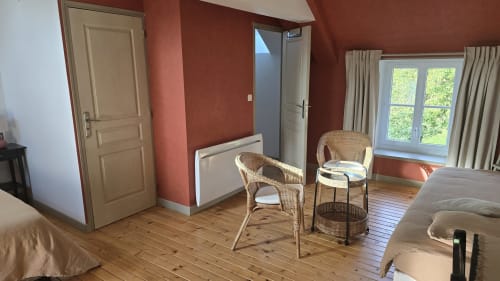Chambre spacieuse aux murs terre cuite, parquet, fauteuils en osier et vue sur jardin au Domaine de la Cour VAUTIER