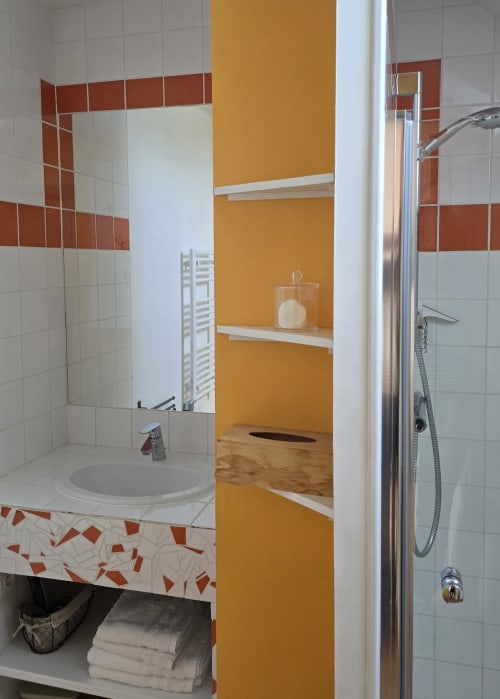Salle de bain moderne avec carrelage blanc, accents rouges, mur jaune, lavabo, miroir et douche au Domaine de la Cour VAUTIER