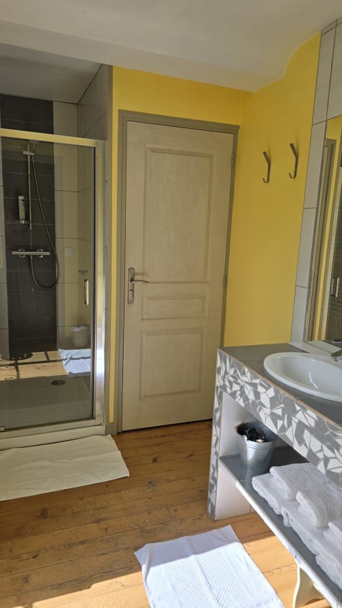 Salle de bain moderne aux murs jaunes, lavabo, meuble en bois et douche à l'italienne à la Domaine de la Cour VAUTIER