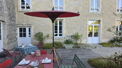 Charmante cour jardin au Domaine de la Cour VAUTIER à Mandeville-en-Bessin avec parasol rouge, tables de restaurant et pierre