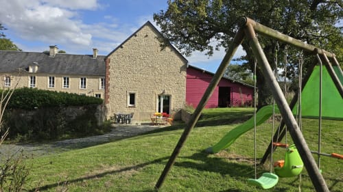 Chaumière en pierre avec balançoire verte dans le jardin paysagé du gîte Domaine de la Cour Vautier en Normandie