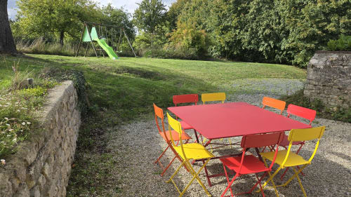 Colorful outdoor dining area with red table and multicolored chairs in the garden at Domaine de la Cour Vautier cottage,