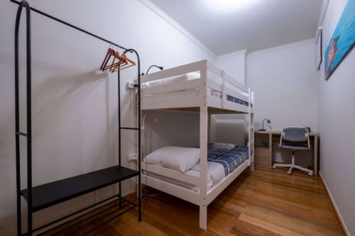 Shared bedroom with white bunk beds, wooden flooring, desk, and clothing rack at EcoHost apartment in Porto