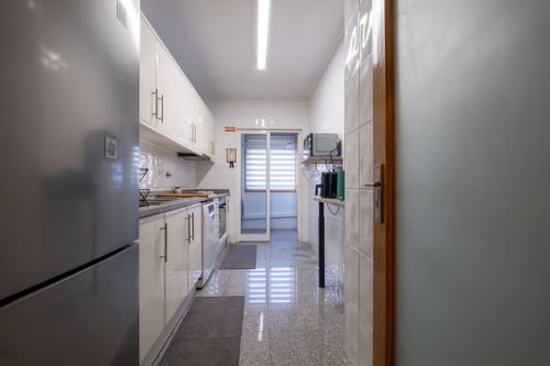Modern galley kitchen in EcoHost apartment, Porto. White cabinetry, stainless steel appliances, glossy floor.