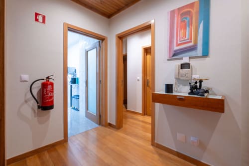 Modern hallway at EcoHost Porto apartment with wooden doors, fire extinguisher, reception desk, and colorful abstract artwork