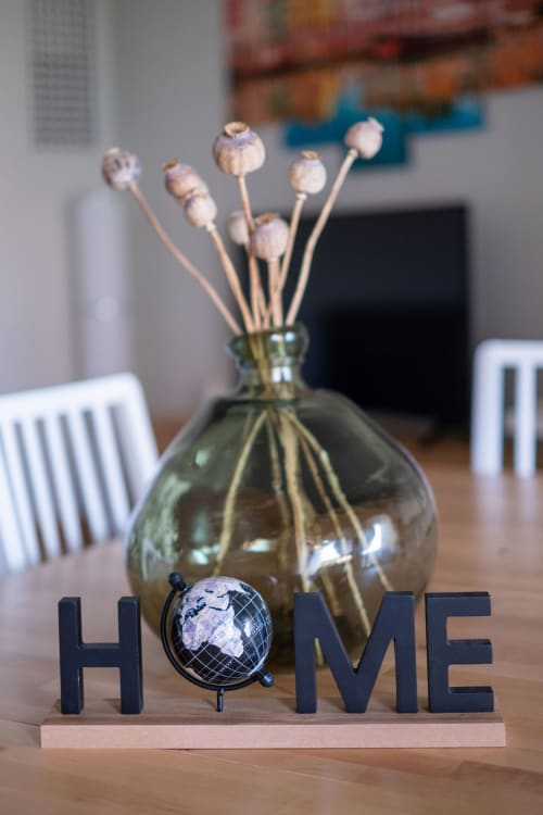 HOME sign with decorative globe and dried flowers in vase on wooden table at EcoHost apartment