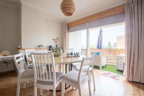 Modern dining area with white chairs at round table, overlooking Porto terrace and garden in FamilyHub apartment