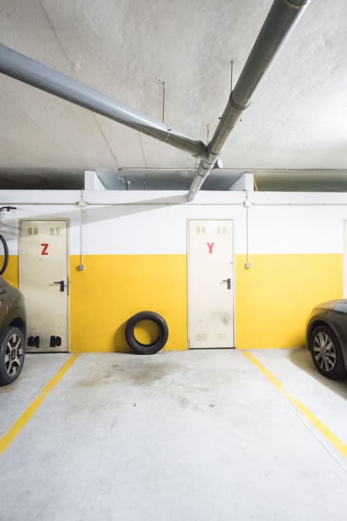 Underground parking garage at EcoHost with yellow-marked spaces, concrete ceiling, and metal pipes in Senhora da Hora, Porto