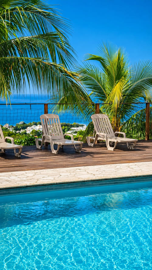 Terrasse piscine de l'hôtel Paradis Tropical à Baillif avec transats, palmiers, vue sur l'océan et eau cristalline