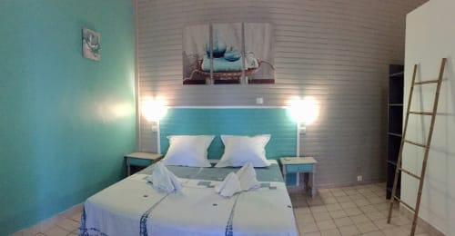 Chambre à l'hôtel Paradis Tropical à Baillif avec lit queen-size, accents turquoise, literie blanche, éclairage moderne et style tropical