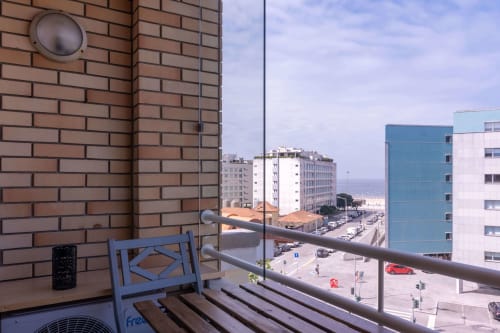Balcony view from OceanBreeze apartment in Matosinhos showing blue chair, railing, and coastal town with buildings and beach
