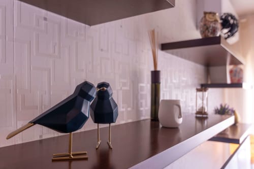 Minimalist black bird sculptures on dark table in modern EcoHost apartment with white geometric wallpaper and sea view