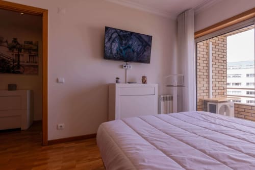 Modern bedroom in EcoHost Matosinhos with lavender walls, queen bed, wall-mounted TV, wooden flooring, and sea views from