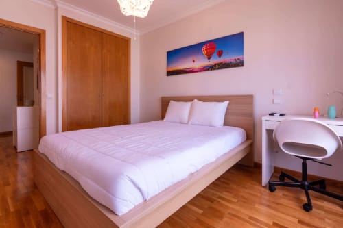 Modern pink bedroom with wooden bed, desk, and hot air balloon artwork at EcoHost beachfront apartment in Matosinhos