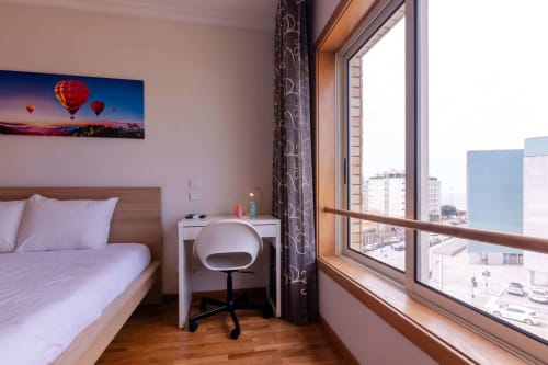 Modern bedroom at EcoHost Matosinhos with sea view, bed, desk, chair, and large window overlooking city and ocean