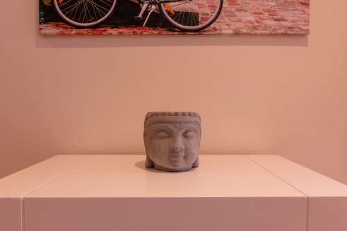 Stone Buddha head sculpture on white pedestal in EcoHost apartment with bicycle artwork and coral pink walls in Matosinhos.