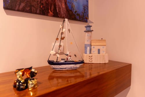 Coastal décor on wooden shelf: sailboat model, lighthouse figurine, and decorative anchor at EcoHost Matosinhos apartment.