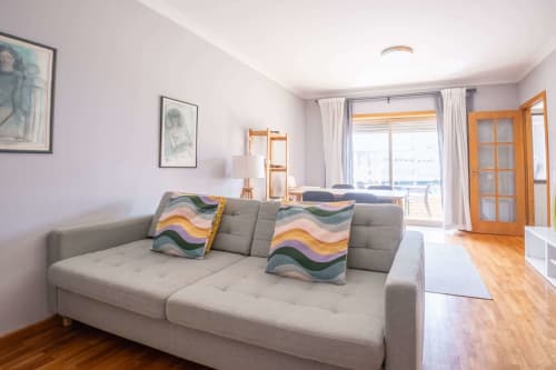 Modern living room with gray sofa at EcoHost Matosinhos apartment, city views through glass doors to balcony