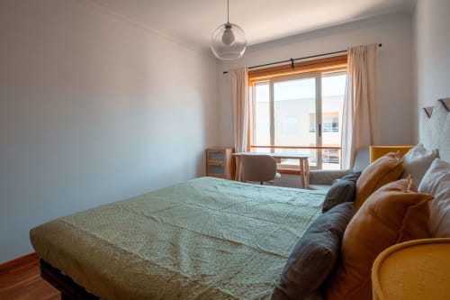 Bright bedroom at EcoHost Matosinhos with queen bed, leather seating, pendant light, and ocean-view balcony