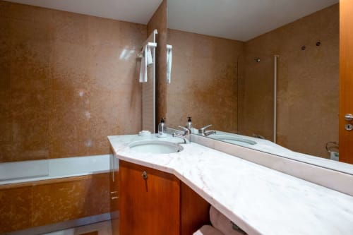 Modern bathroom at EcoHost Matosinhos with marble countertop, white sink, wooden vanity, brown tiled walls, and large mirror