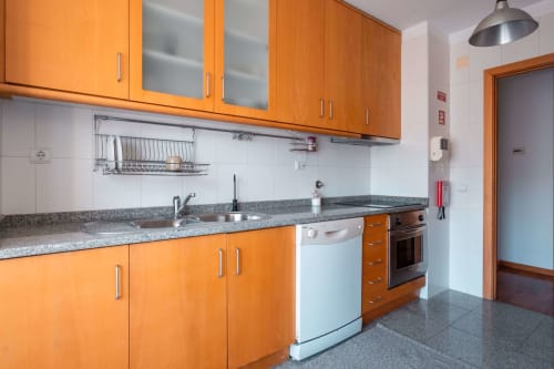 Modern kitchen with orange cabinets, gray countertop, and stainless steel appliances at EcoHost apartment in Matosinhos,