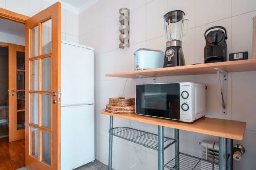 Modern kitchenette at EcoHost Matosinhos with microwave, blender, coffee maker, and storage shelves