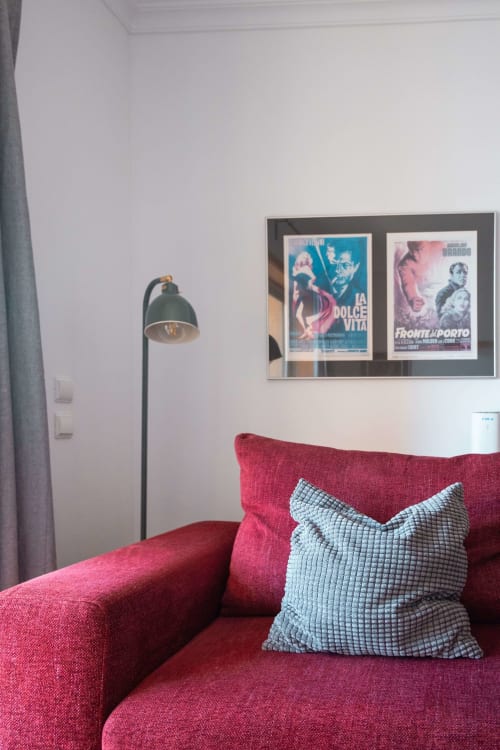 Red sofa with blue cushions in EcoHost apartment, vintage Italian film posters on wall, arc lamp, Matosinhos accommodation