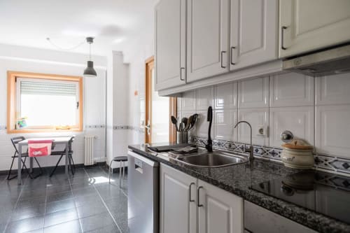 Modern kitchen with white cabinets, black granite countertop, and stainless steel sink at Gaia Beach&Golf apartment in