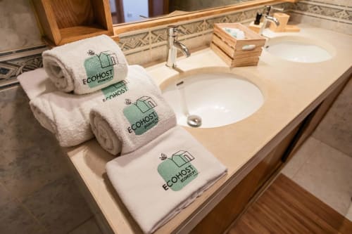 EcoHost branded towels arranged on bathroom vanity with dual sinks and wooden accents at Gaia Beach&Golf apartment in