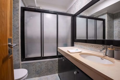 Modern bathroom with double sink, black framed shower enclosure, gray tile walls at EcoHost Gaia Beach&Golf apartment in