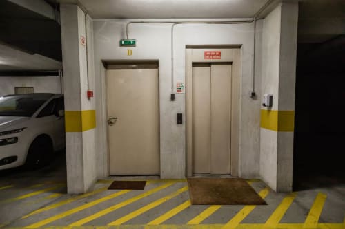 Underground parking garage with two beige elevators, yellow safety markings, and a white car visible at EcoHost in Arcozelo,