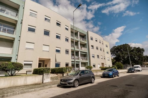 Modern apartment building in Arcozelo with parked cars, balconies, and green landscaping on sunny day
