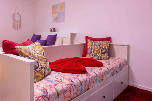 Colorful child's bedroom at EcoHost with pink walls, white bed, red and patterned pillows, and wall decorations.