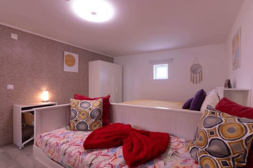 Bright pink bedroom with two beds, colorful pillows, white wardrobe, and brick accent wall at Perafita Yellow House