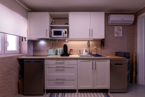 Modern pink kitchen with stainless steel appliances, wood countertop, brick walls, and air conditioning in Perafita apartment