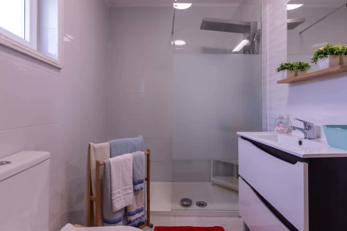 Modern bathroom in Perafita Yellow House with walk-in shower, vanity sink, and wooden towel rack with rolled towels