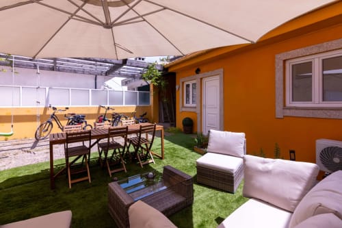 Sunny patio at Perafita Yellow House with dining table, lounge seating, umbrellas, bicycles, and orange house backdrop
