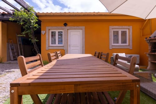 Wooden outdoor dining table with chairs in garden courtyard of Perafita Yellow House, featuring bright orange walls and