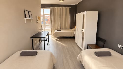 Shared room at Banama Coliving hostel in Corralejo with twin beds, desk, wardrobe, and balcony access